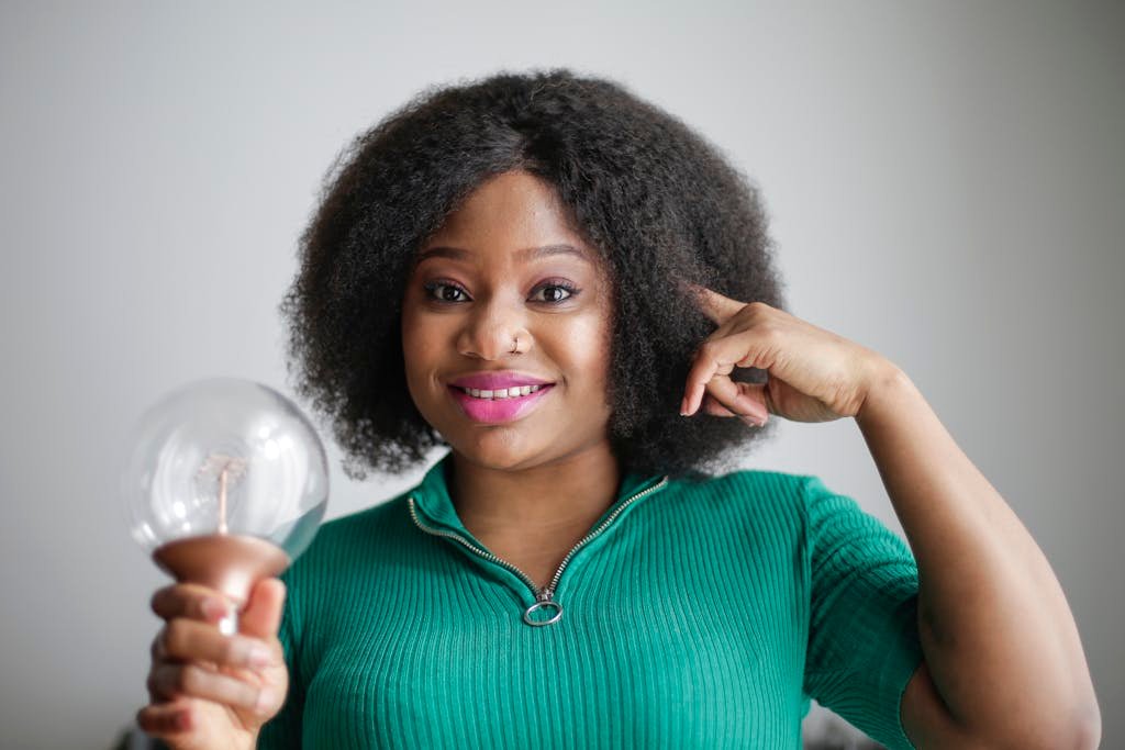 Positive young African American lady holding light bulb in hand on gray background